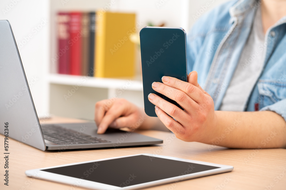 Fototapeta premium Close up of student girl hands using multiple devices sitting on a desk at home