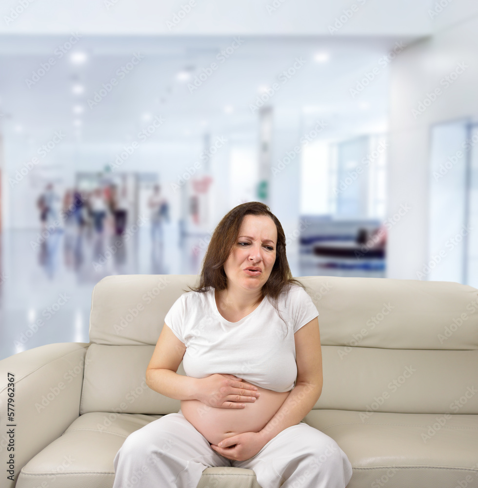 Pregnant woman suffering belly ache sitting on a couch in a hospital Pregnant woman suffering belly ache sitting on a couch in a hospital