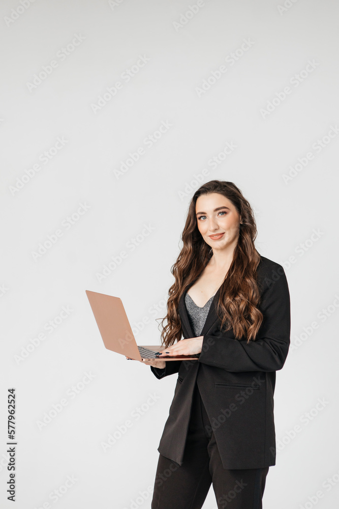 Curly adult business lady in elegant jacket standing while working on laptop against gray background Curly adult business lady in elegant jacket standing while working on laptop against gray background