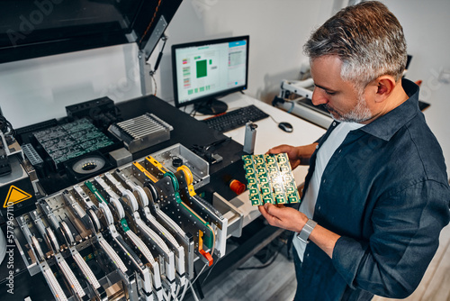 A man holds a microcircuit near a machine that develops chips for electronics maintenance. photo