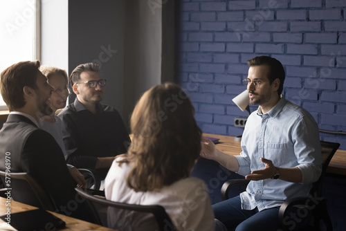 Business group brainstorming on meeting in office. Team leader man speaking to employees, explaining tasks, ideas. Teambuilding coach training staff. Therapy group sitting in circle, talking