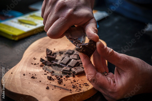 Chopping dark chocolate on a wooden cutting board with small metal knife