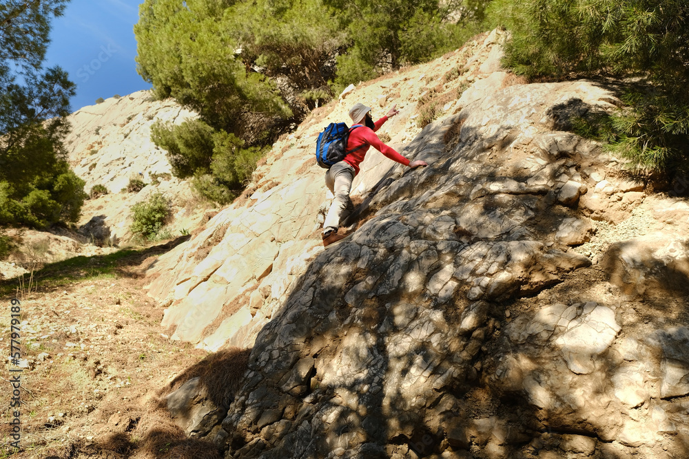 young tourist, man in orange jacket with backpack climbs cliff, rock climber, extreme people lifestyle, mountaineering, concept of reach goal, life insurance, difficulties in hike, extreme sports