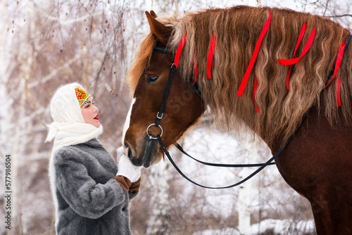 Russian beauty girl in traditional clothes  with red big horse in forest winter. They look at each other.