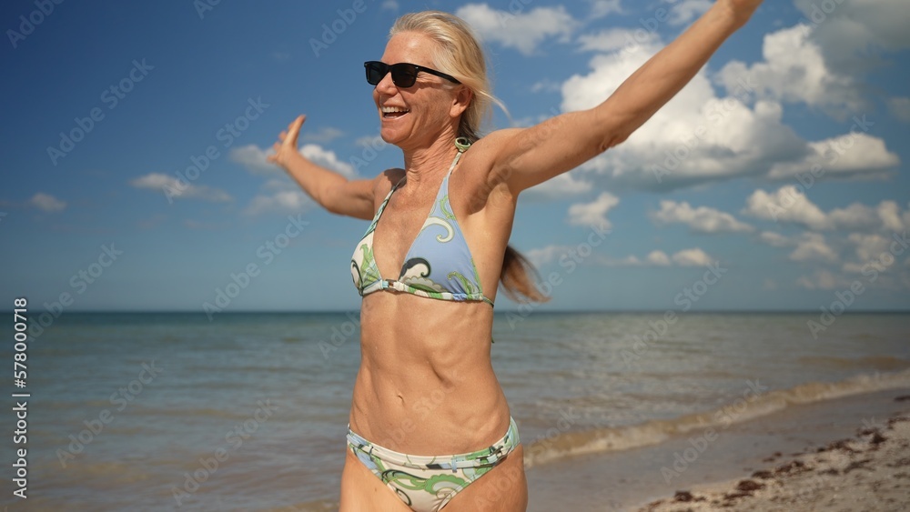 Closeup of smiling blissful woman running arms outstretched at sunset on beach. Mature senior woman enjoying carefree freedom as a winner. Happiness, freedom, success Closeup of smiling blissful woman running arms outstretched at sunset on beach. Mature senior woman enjoying carefree freedom as a winner. Happiness, freedom, success