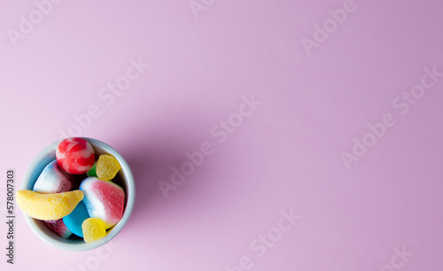 Bol relleno de gominolas multicolores y caramelos sobre fondo rosa con espacio para texto