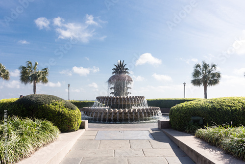 Pineapple Fountain, from mid-distance, Charleston Riverfront Park, Charleston, South Carolina. Looking east with walkway, blue sky, clouds, and palmetto trees. No people.