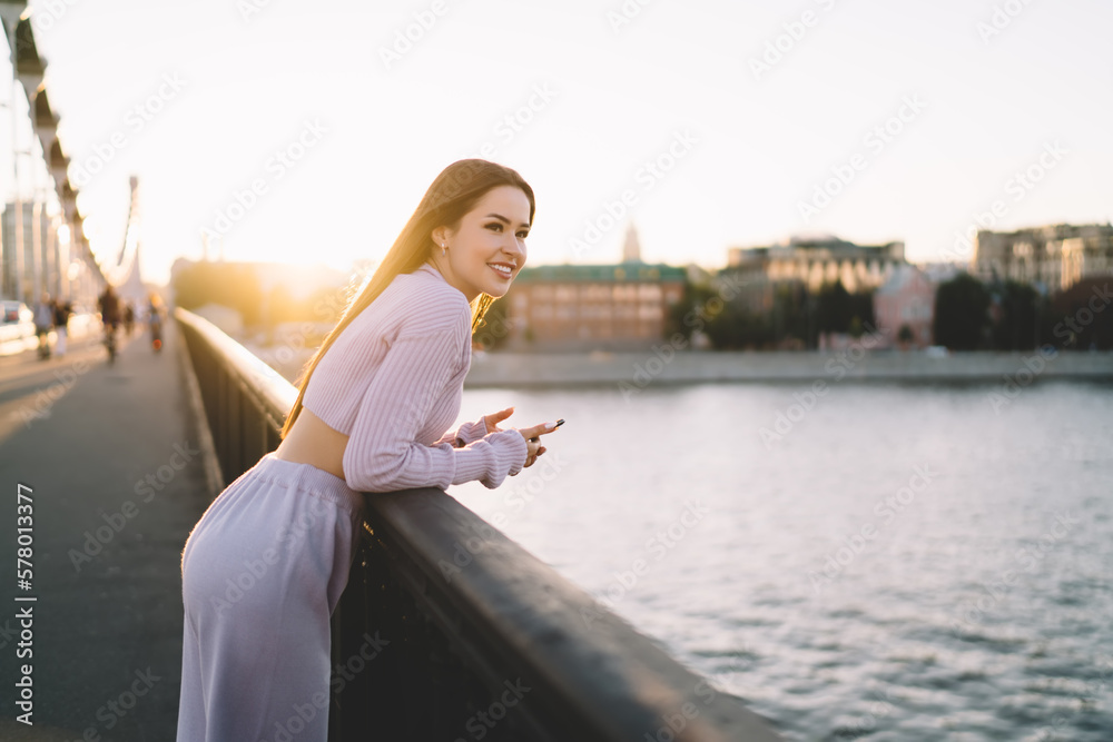 Happy female millennial browsing mobile phone on bridge