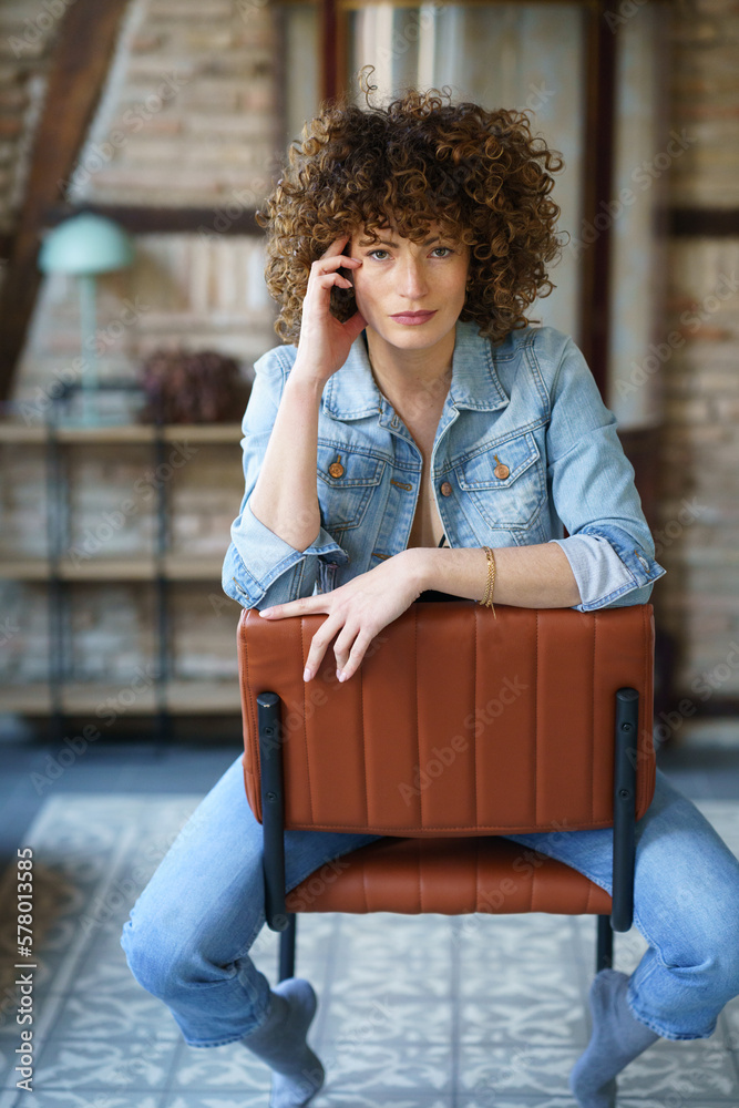 Smiling woman in denim jacket and jeans sitting on chair Stock Photo ...