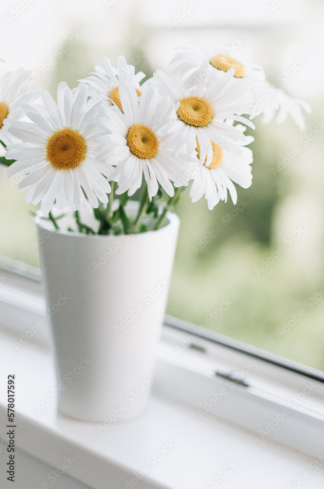White vase with big daisies on the balcony.