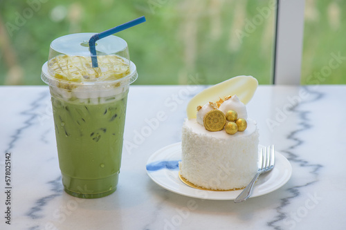 Ice matcha green tea in plastic cup and Coconut cake decorated with golden leaf, biscuits and white chocolate