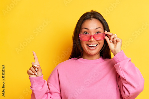 Fotografija Portrait of surprised pretty young asian woman in pink sweater pointing index fi