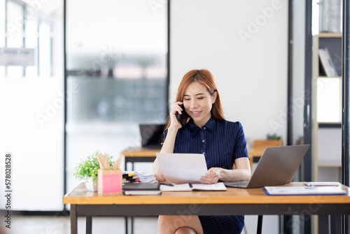 Cheerful business Asian woman freelancer making telephone call share good news about project working in office workplace, business finance concept.   © David
