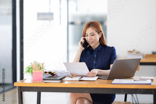 Cheerful business Asian woman freelancer making telephone call share good news about project working in office workplace, business finance concept. 