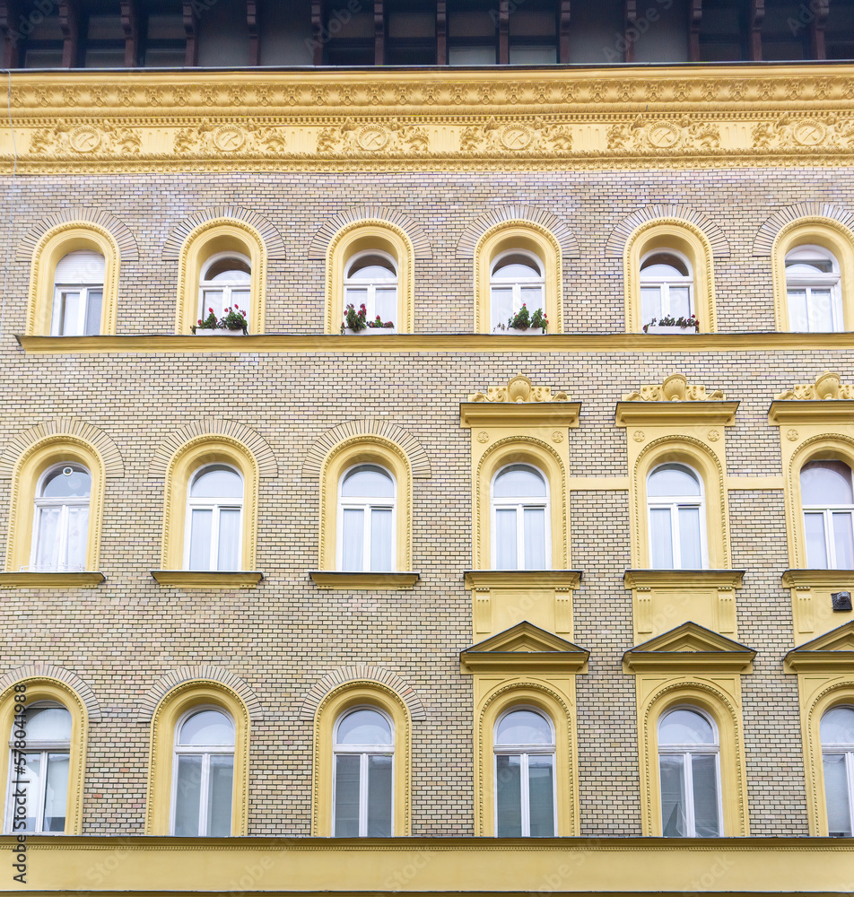 An old yellow brick house with beautiful stucco and flowers on the windowsills, in the historical center of Budapest, Hungary. An old yellow brick house with beautiful stucco and flowers on the windowsills, in the historical center of Budapest, Hungary.