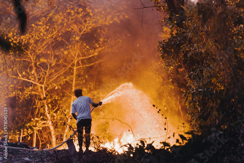 A man stands with his back and extinguishes a fire in a rainforest with a hose © asokova