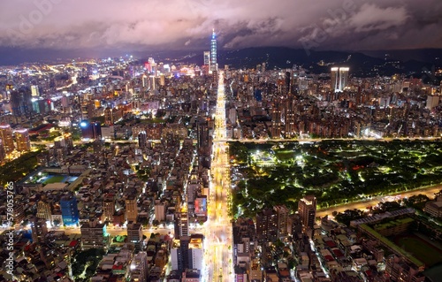 Night skyline of Taipei City, the vibrant capital of Taiwan, with 101 Tower standing out amid high-rise buildings in Xinyi Commercial District and Daan Forest Park enclosed by avenues under cloudy sky