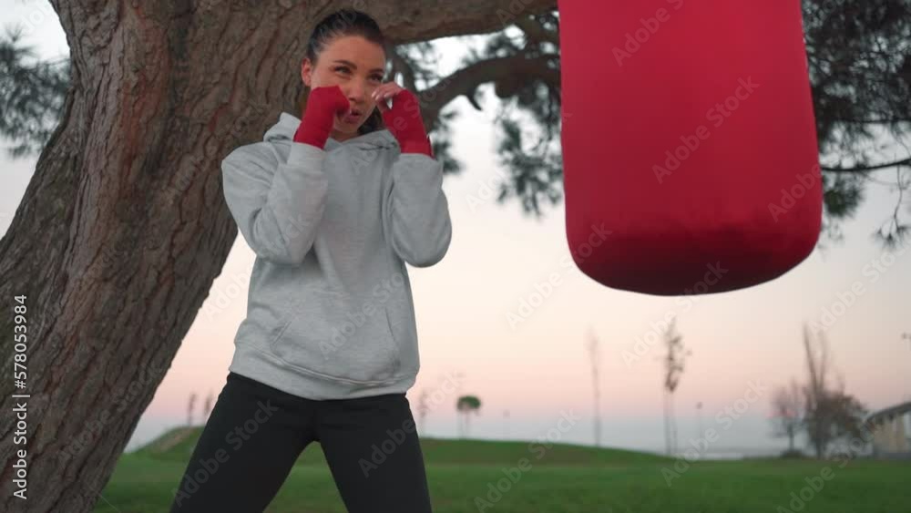 Fitness woman training boxing punching bag outside in outdoor gym