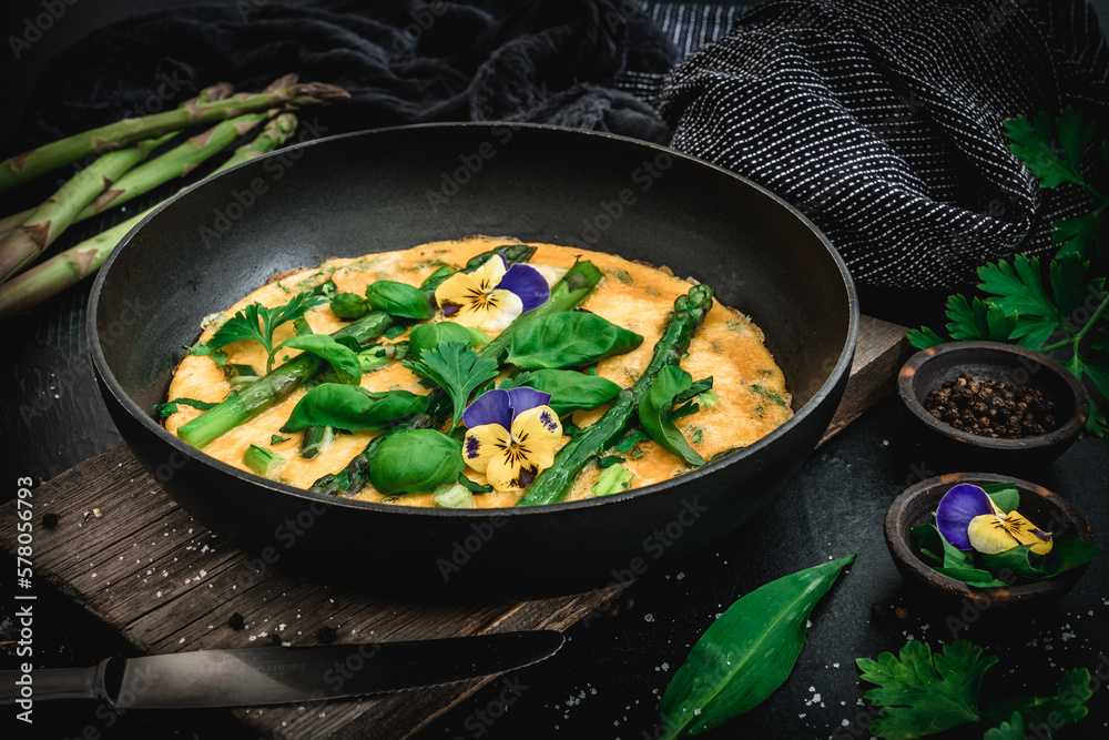 Omelette with green asparagus, basil and herbs on black background