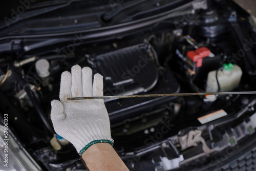 A gloved mechanic's hand is holding an oil dipstick to check the engine oil level. photo