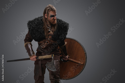 Portrait of violent barbarian from north with deerskin and armor against gray background.