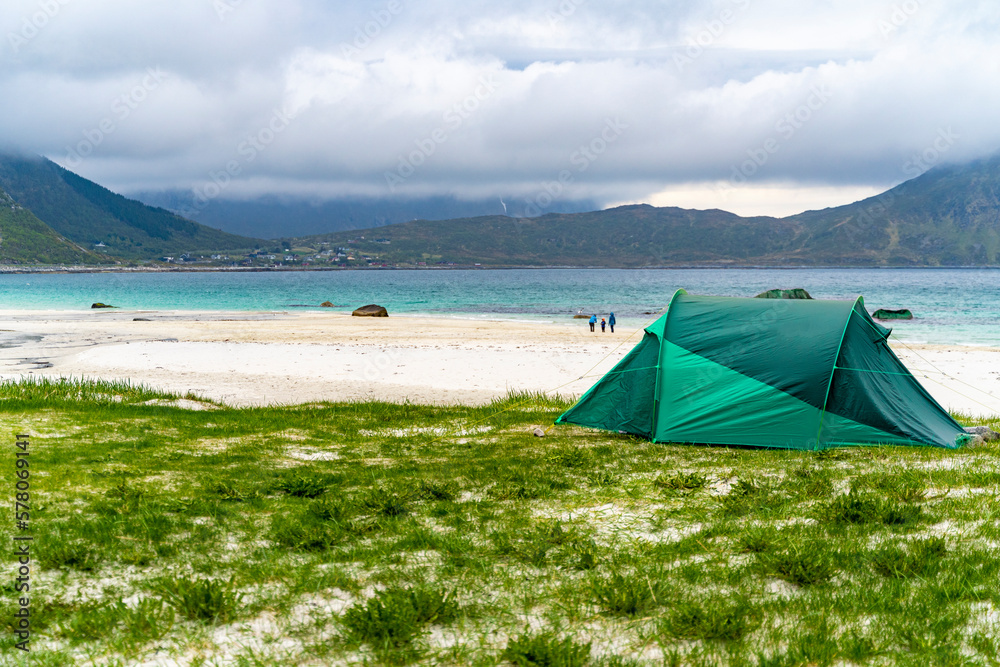 Tent on a Lofoten beach in Norway with sea and mountain views, during a cloudy spring day, copy space