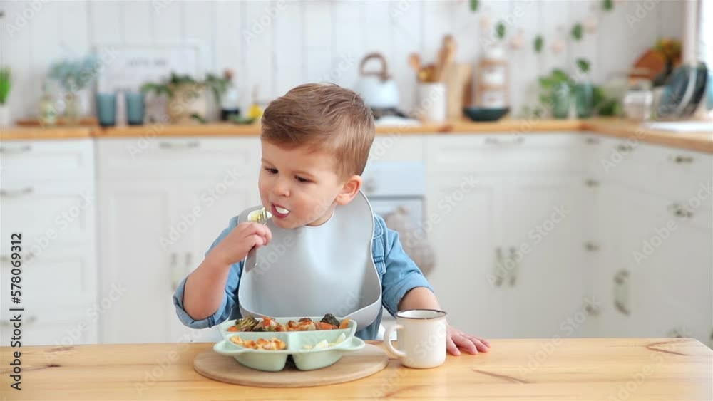 Adorable caucasian toddler boy eats boiled eggs on his own, pricking them on fork. The concept of self-feeding. BLW. Child eats healthy vegetables with meat on a high chair. Mock up. Place for text Adorable caucasian toddler boy eats boiled eggs on his own, pricking them on fork. The concept of self-feeding. BLW. Child eats healthy vegetables with meat on a high chair. Mock up. Place for text