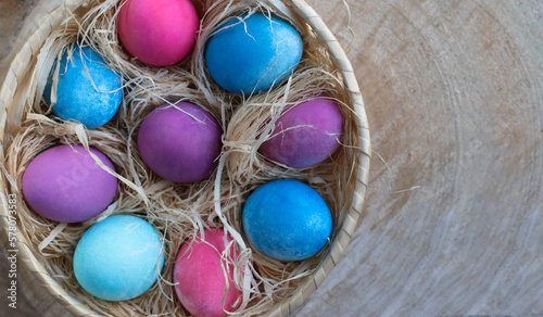 Happy Easter holiday. Bright colored eggs in a nutural basket with hay on a wooden cut natural background. Spring Easter concept in eco style. Top view. Copy space