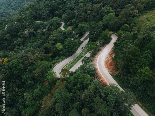 Aerial view of countryside road passing through the green forrest and mountain