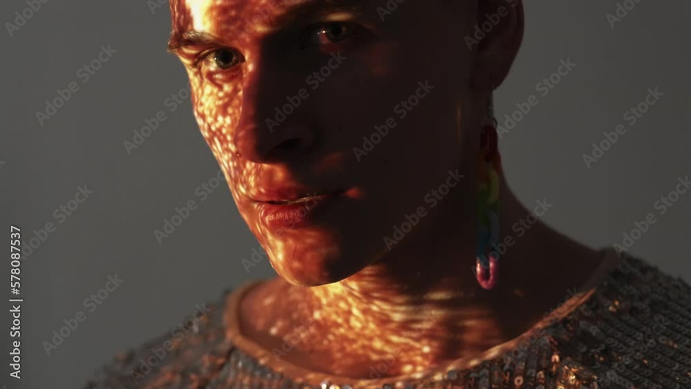 Lgbtq style. Binary male. Double exposure portrait. Handsome man in spangle shirt rainbow color plastic earrings posing gray in golden shining light sparkles overlay background. Lgbtq style. Binary male. Double exposure portrait. Handsome man in spangle shirt rainbow color plastic earrings posing gray in golden shining light sparkles overlay background.