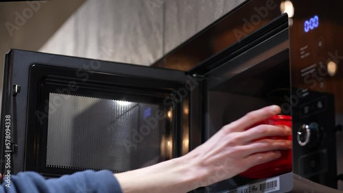 A man puts food in the microwave to heat up. Semi-finished products, fast food. Microwave and male hands close-up photo