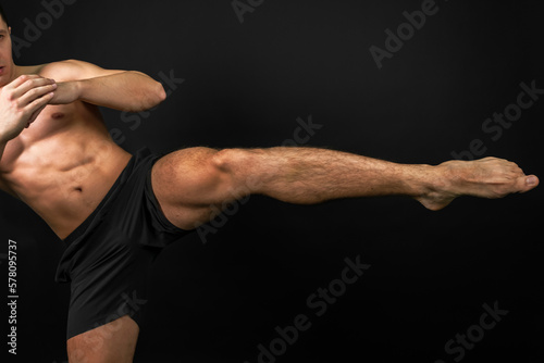 Portrait of a muscular Boxer kicking on an isolated black background. Boxer strikes with his foot.
