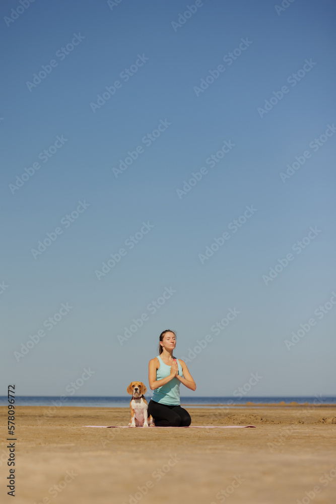 woman and dog meditate on yoga mat on ocean in morning. sports outdoor for mental and physical health, breathing and physical practices. taking care of the body, spine and muscles