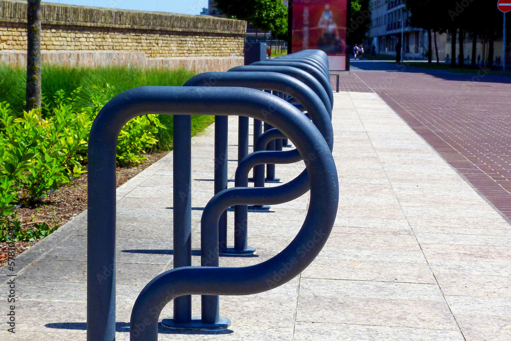 bent steel pipe bicycle racks in urban setting in diminishing perspective. light gray concrete pavement and interlocking brick paving. green park and brick wall. abstract low angle view. city square.