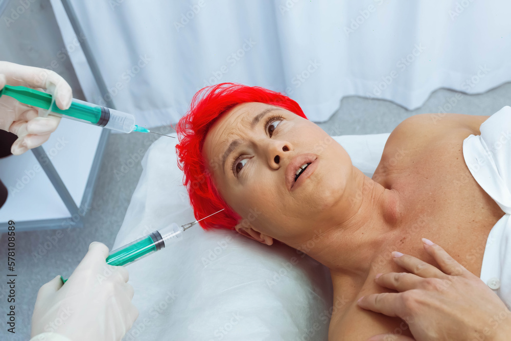 Naklejka premium Woman with a short bright red hair in a white room lying on a treatment table and hands reaching out to her with needles.