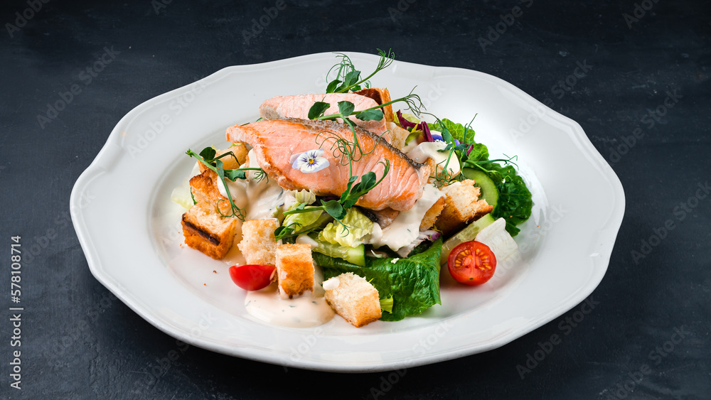 Italian food Caesar salad with salmon, parmesan cheese, lettuce, cucumbers, tomatoes, croutons on a dark table. Italian food Caesar salad with salmon, parmesan cheese, lettuce, cucumbers, tomatoes, croutons on a dark table.