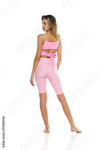 a young barefeet woman in pink short leggings and top posing on a white background. Back, Rear View