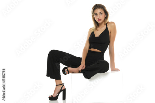 a young woman in black wide trousers and bra sitting on a white background