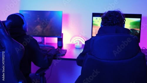 4k video of two young men playing video games with their backs turned and turned to celebrate the successes of the team online. Concept: Video games, diversity, teamwork