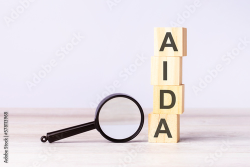magnifying glass and wooden blocks with text AIDA on wood table, grey background © Maks_Lab