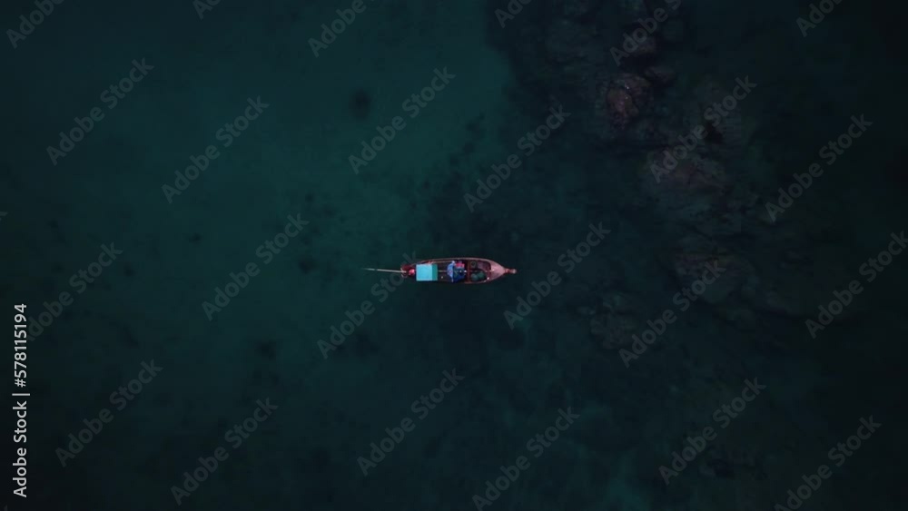 Wooden longtail boat is moored in the sea next to rocky coast and two people in kayak are paddling nearby filmed from above by drone. Aerial footage of boat floating on the ocean above reef bottom Wooden longtail boat is moored in the sea next to rocky coast and two people in kayak are paddling nearby filmed from above by drone. Aerial footage of boat floating on the ocean above reef bottom