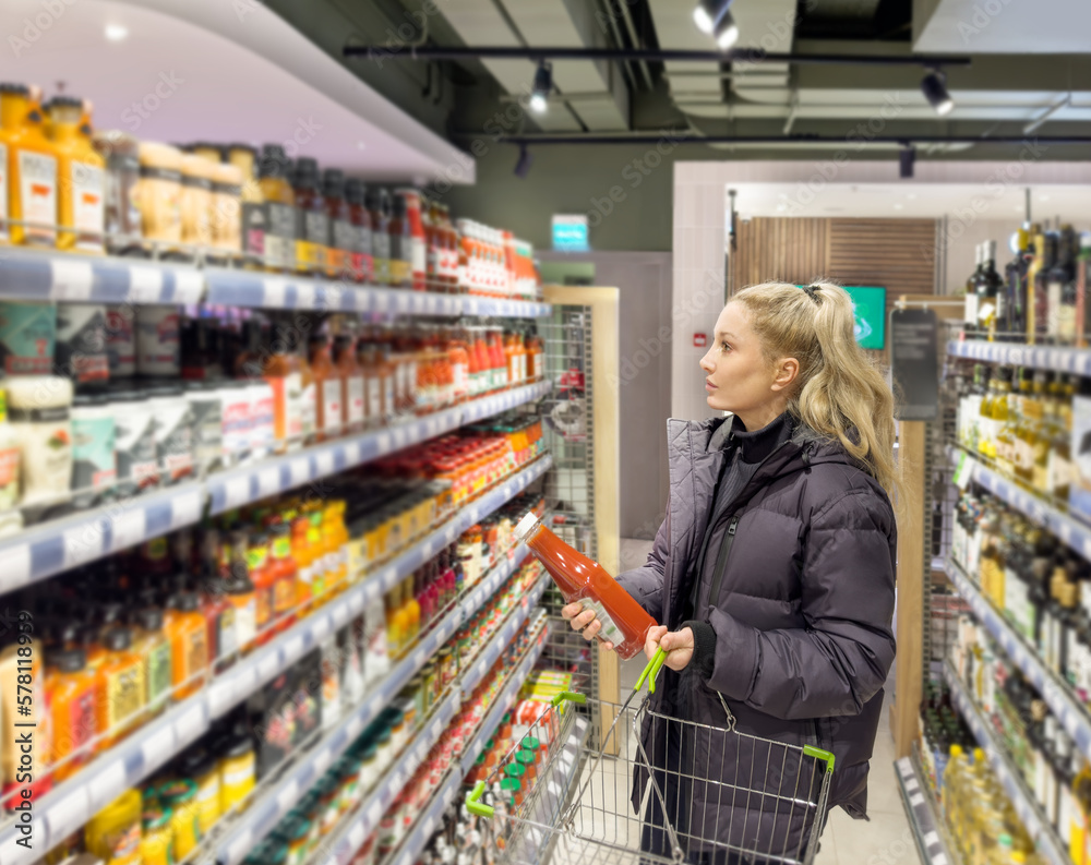 Young woman shopping in supermarket, reading product information.