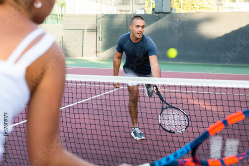 Man in t-shirt playing tennis against woman on court. Racket sport training outdoors.
