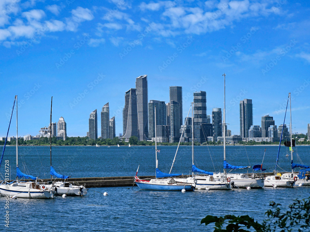 Small sailboats tied up beside breakwater in Lake Ontario, with Toronto suburban apartment building skyscrapers in the background