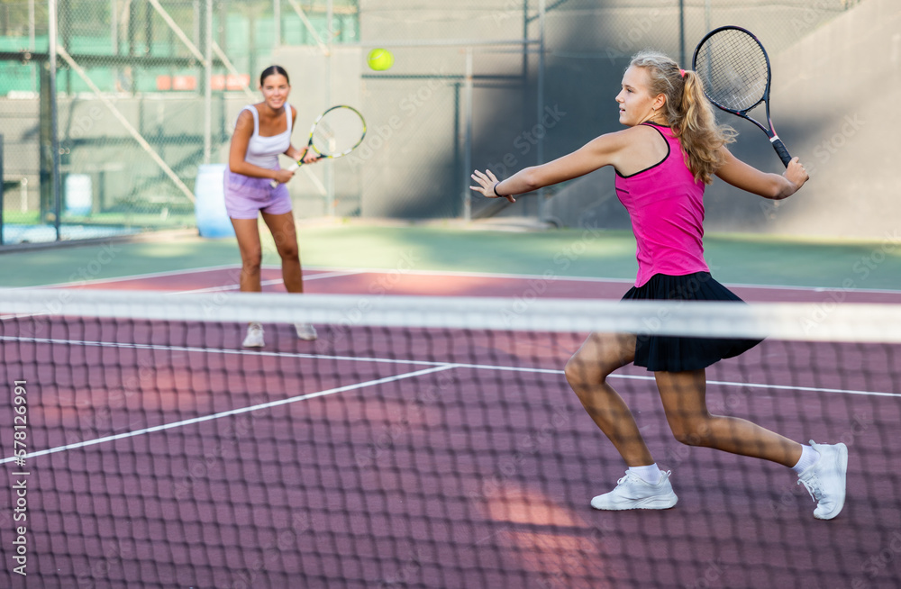Sportive caucasian girl in pink t-shirt and skirt with racquet playing tennis at court