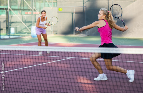 Sportive caucasian girl in pink t-shirt and skirt with racquet playing tennis at court © JackF