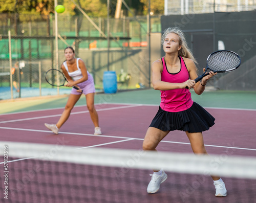 Young beautiful girl in pink t-shirt and her female partner playing tennis on court