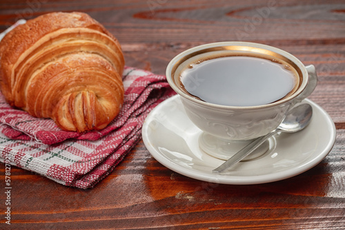 fresh baked croissant and cup of coffee on wooden table.