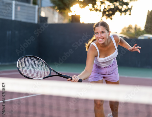 Positive young woman in shorts playing tennis on court. Racket sport training outdoors.