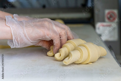 Baker in gloves rolling the dough into a croissant on the table one by one